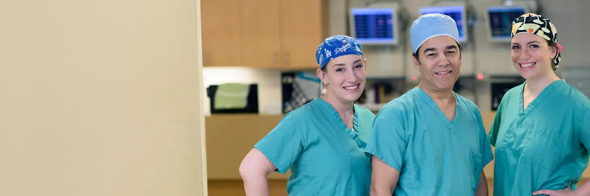 Gastroenterologists Emmy Ludwig, Hans Gerdes, and Robin Mendelsohn, wearing scrubs, smile as they stand together in a procedure suite. 
