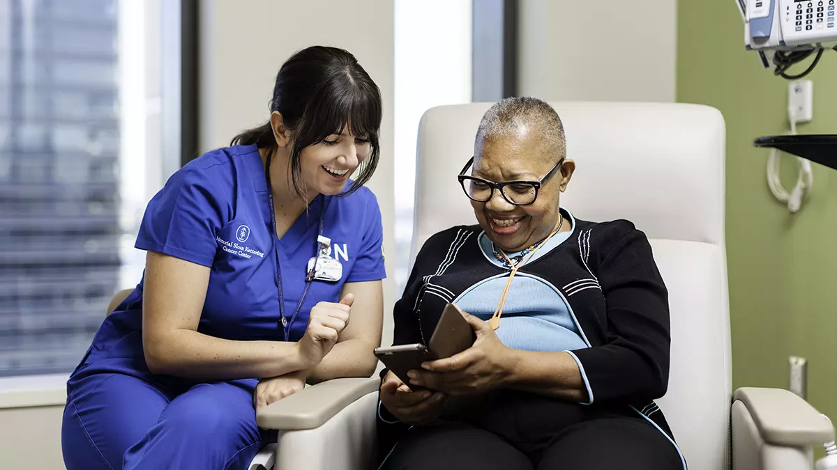 A registered nurse shares a laugh in an exam room with a patient as they both look at a cell phone screen.