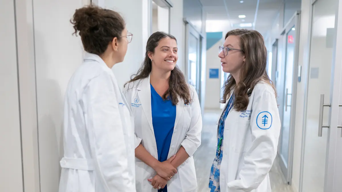 Head and neck surgeon Dr. Jennifer Cracchiolo talks in a hallway with 2 female members of MSK’s head and neck service. 