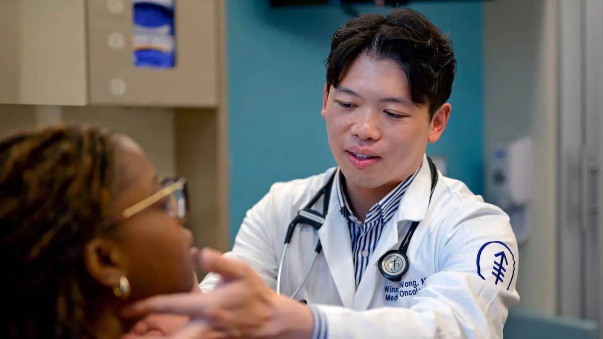 Head and neck medical oncologist Dr. Winston Wong examines the throat of a patient in an exam room  