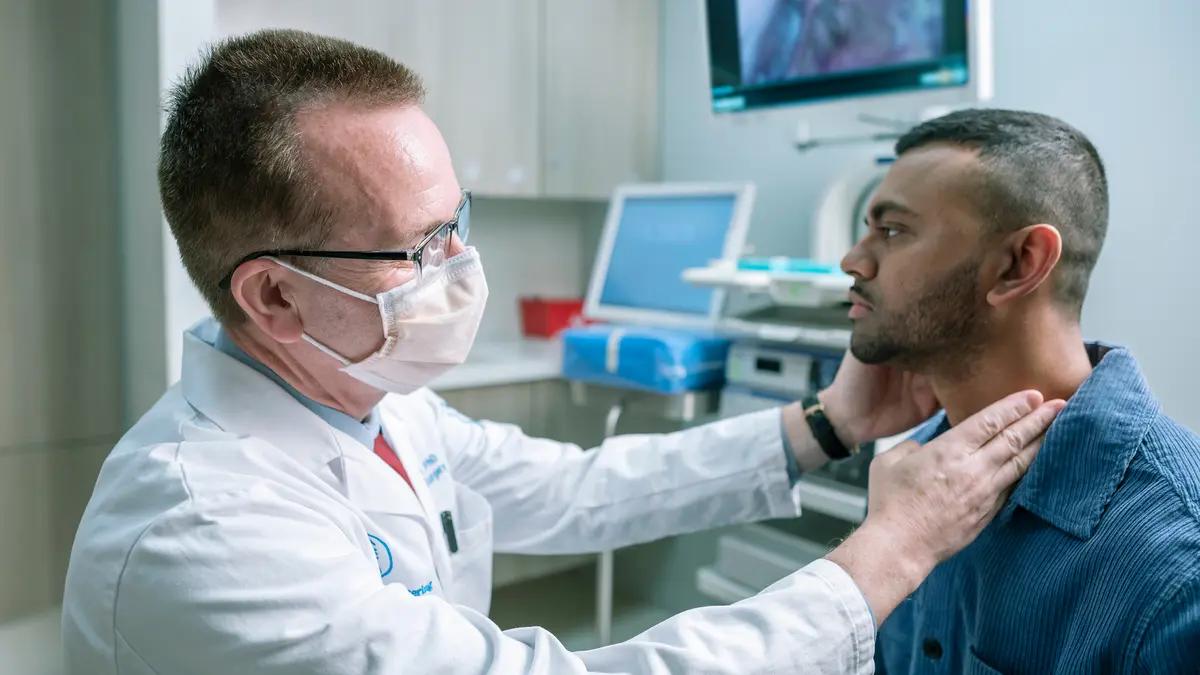 Head and neck surgeon Dr. Ian Ganly feels the throat of an MSK patient in an exam room. 