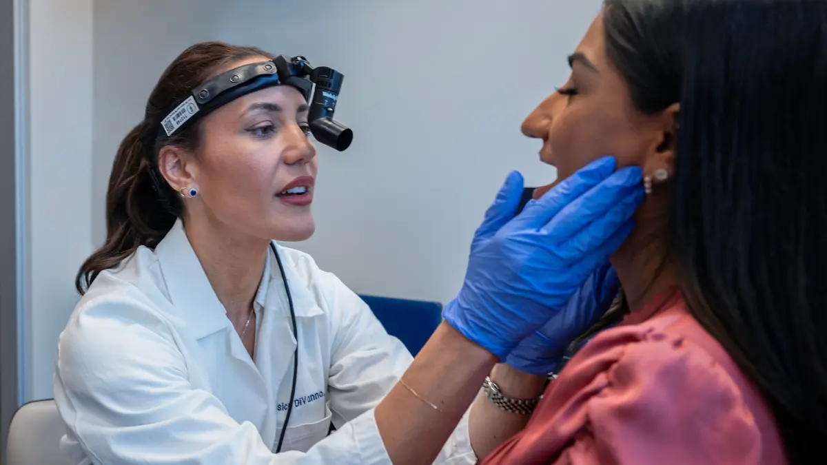 Advanced practice provider Jessica Divanno, wearing a head lamp, examines her patient’s head and neck with gloved hands.  