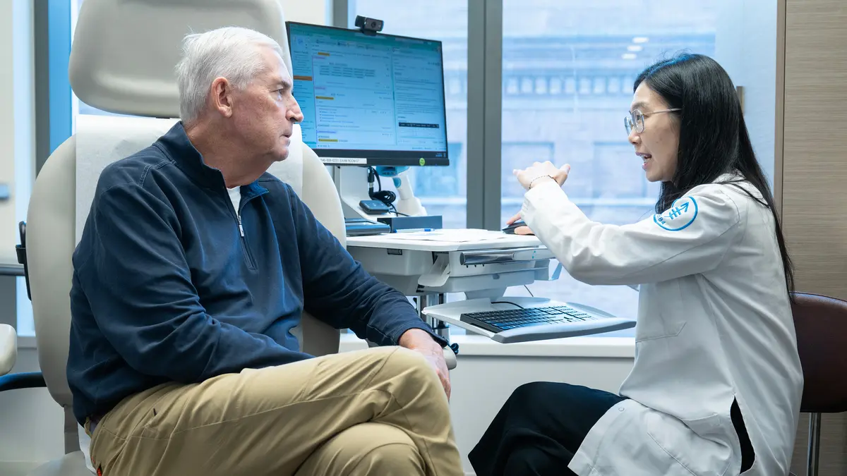 A nurse practitioner is in an exam room talking with a patient who survived head and neck cancer.
