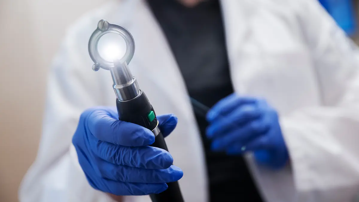 Using gloved hands, a healthcare provider holds a light used to examine a patient. 