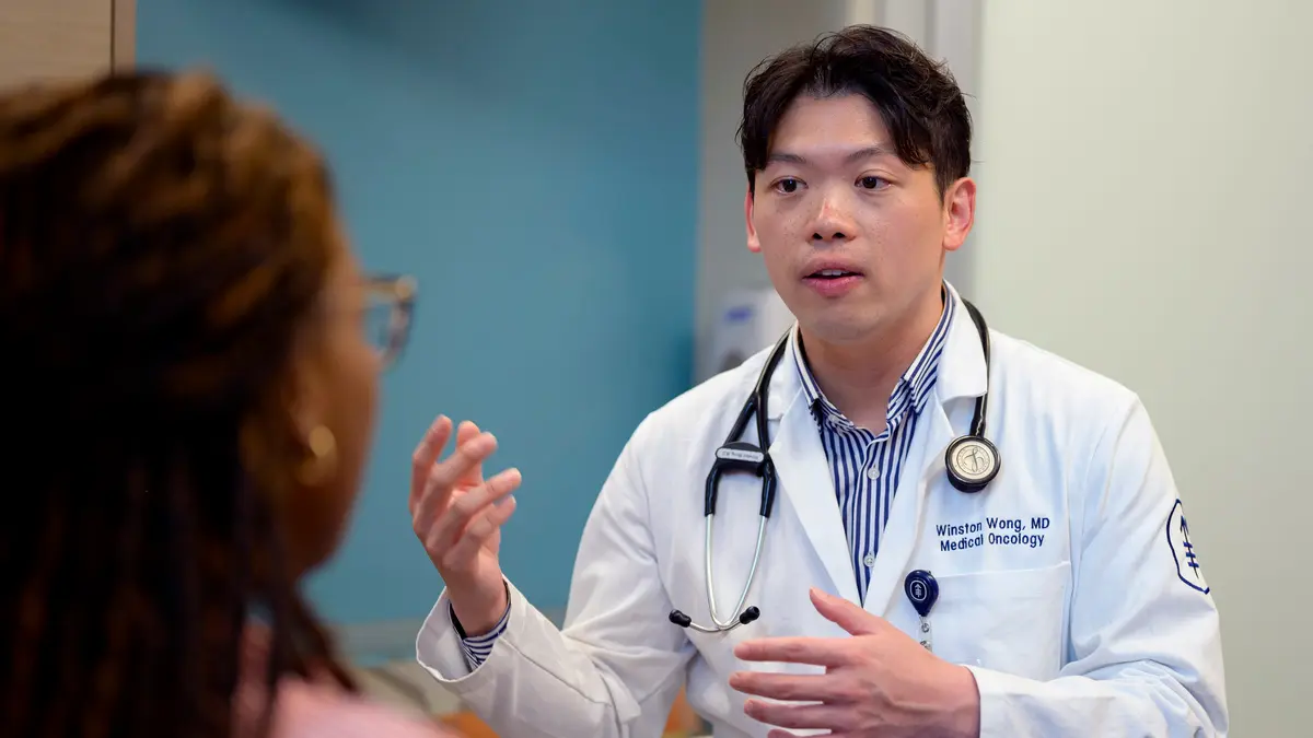 Head and neck medical oncologist Dr. Winston Wong, wearing a white stethoscope, talks with his patient in an MSK exam room. 