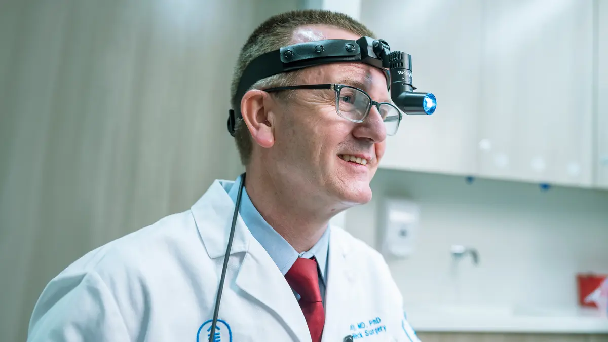 Head and neck surgeon Dr. Ian Ganly, wearing a medical head lamp, is in an MSK exam room. 