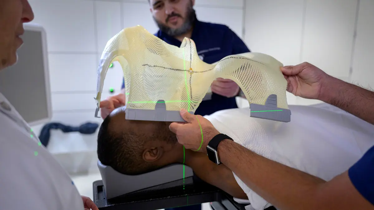 An MSK patient is laying on a machine getting radiation therapy, with 3 people in his care team around him.  