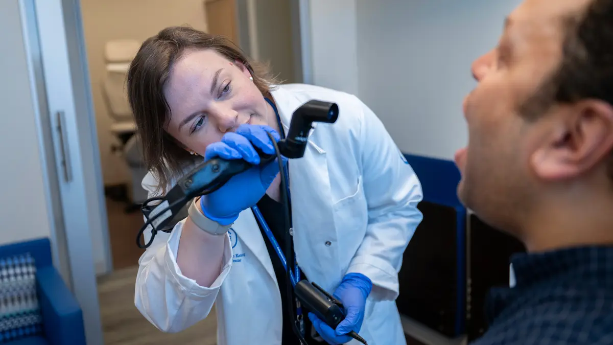 A speech pathologist uses a fiberoptic endoscope to examine her patient’s open mouth. 
